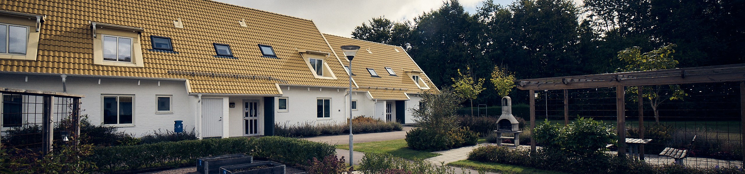 Kedjehus med gult tak och vitfasad med grillplats och odlingslådor