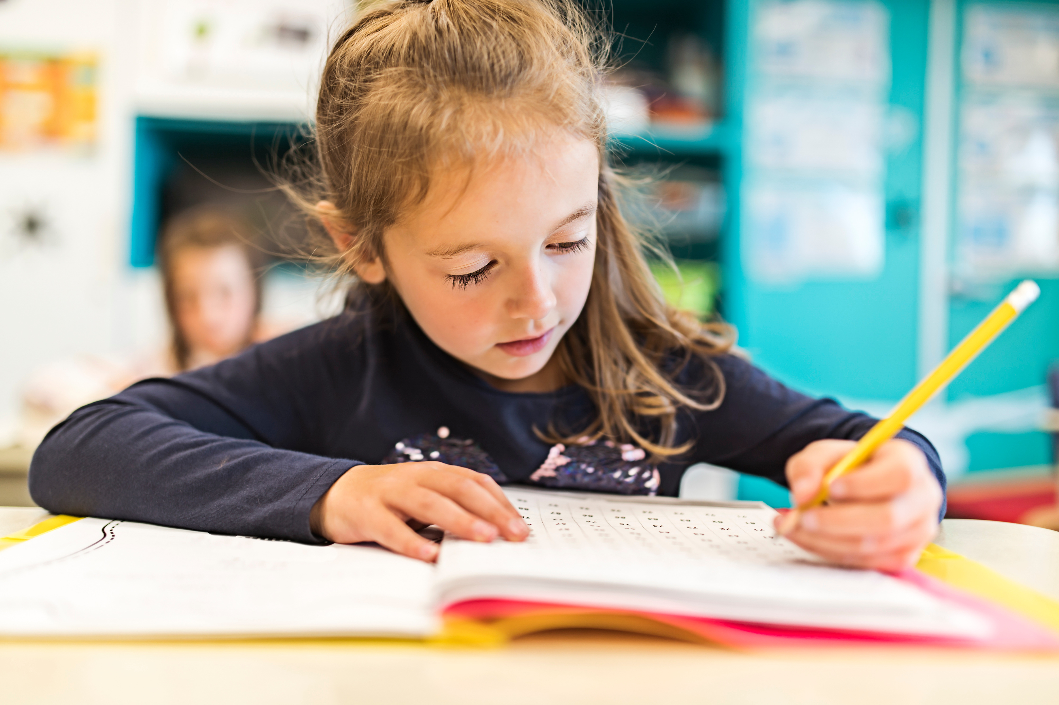 Flicka som sitter och skriver i en textbok i en skolbänk