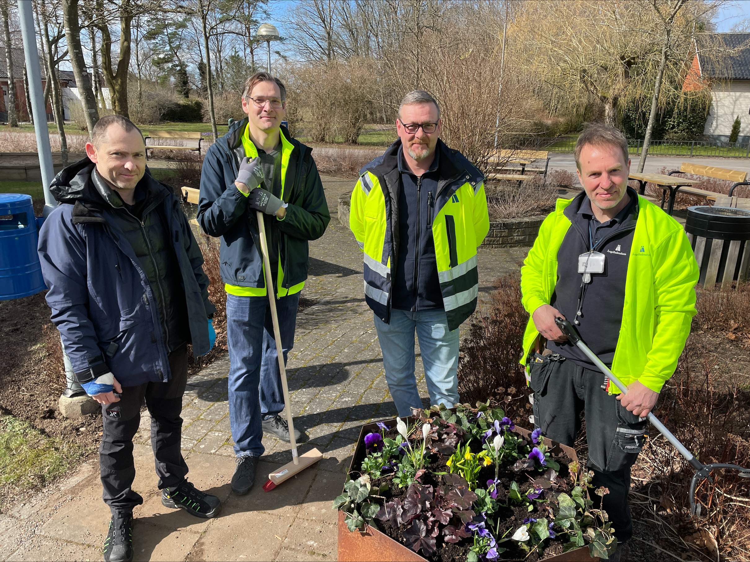 4 medarbetare står utomhus med trädgårdsredskap i händerna.