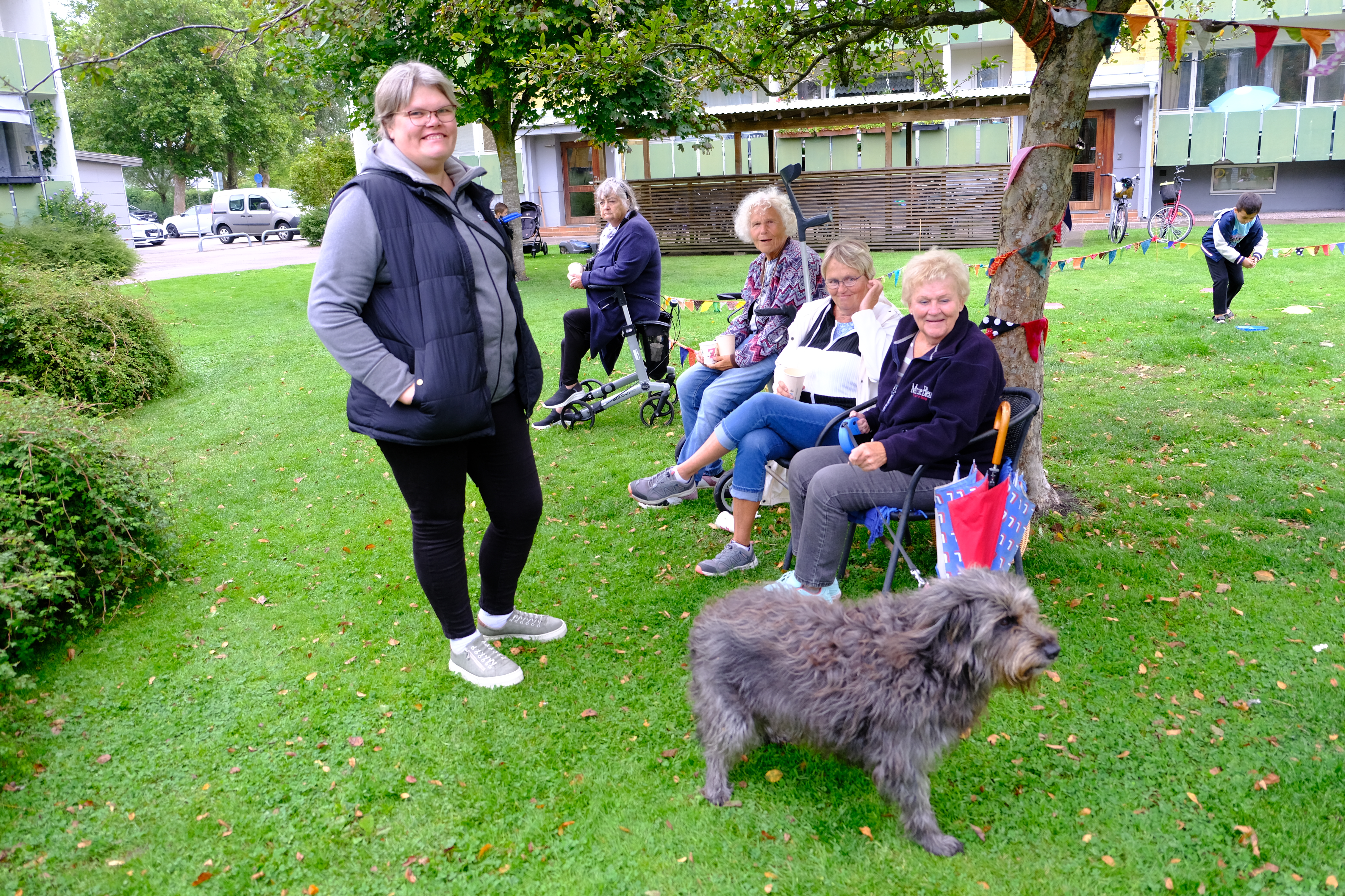 Personer sitter på stolar på en gräsyta, i förgrunden syns en grå hund