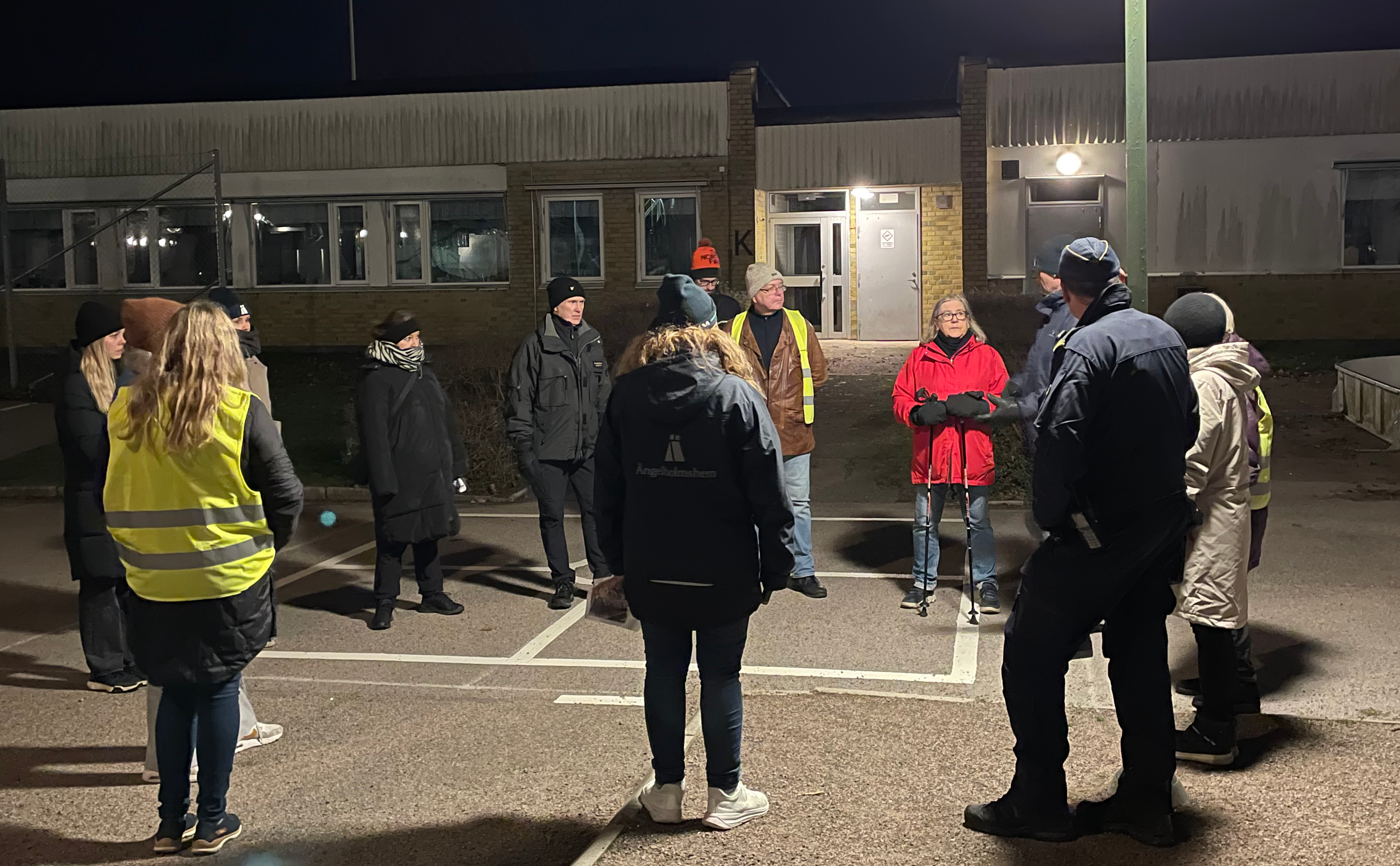 Ett tiotal personer som står utomhus i ring och samtalar kvällstid.
