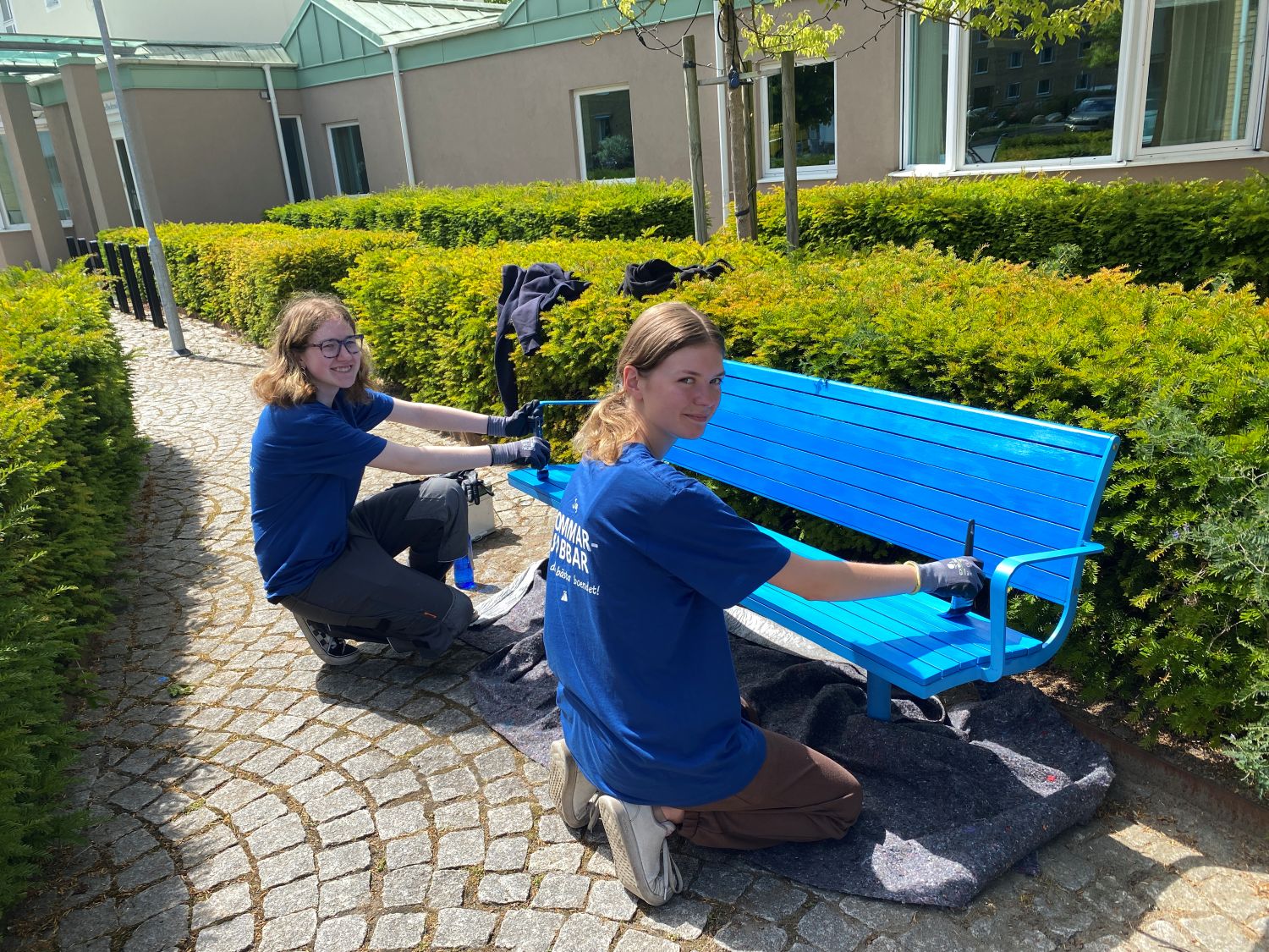 Två sommarjobbare måla en bänk