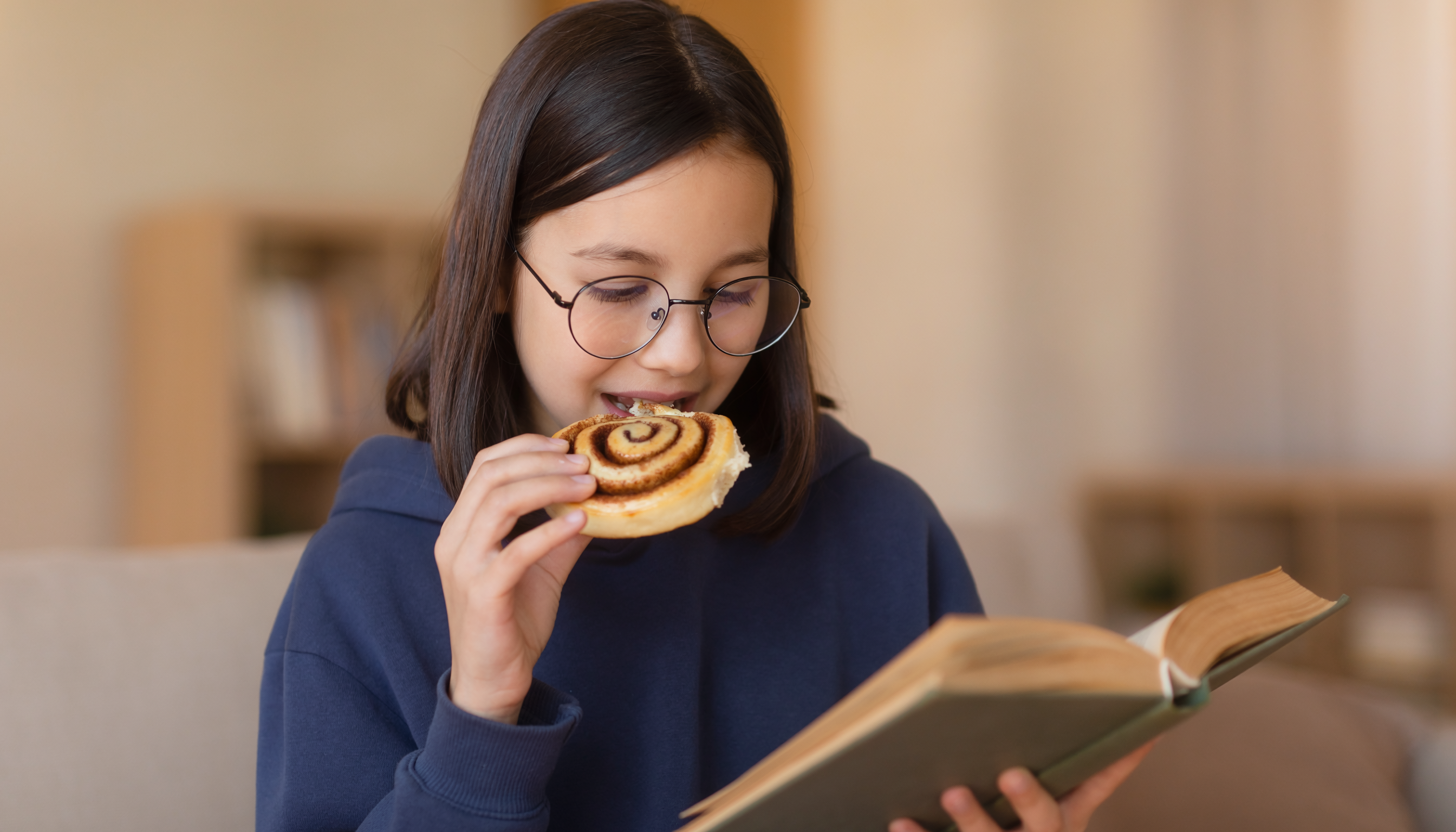 Skolflicka läser bok och äter bulle